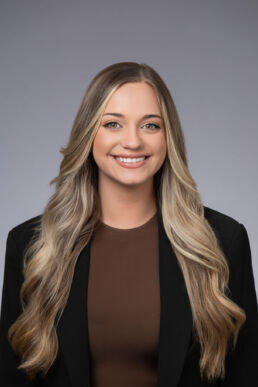 Corporate headshot of female executive in a studio setting against a gray background.