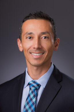 Formal, executive headshot of engineer against dark gray background onsite in Tampa, Florida.