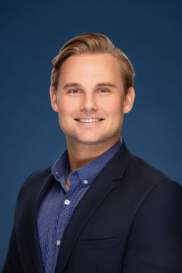 Professional headshot of male executive with blue background for company website in Clearwater, Florida.