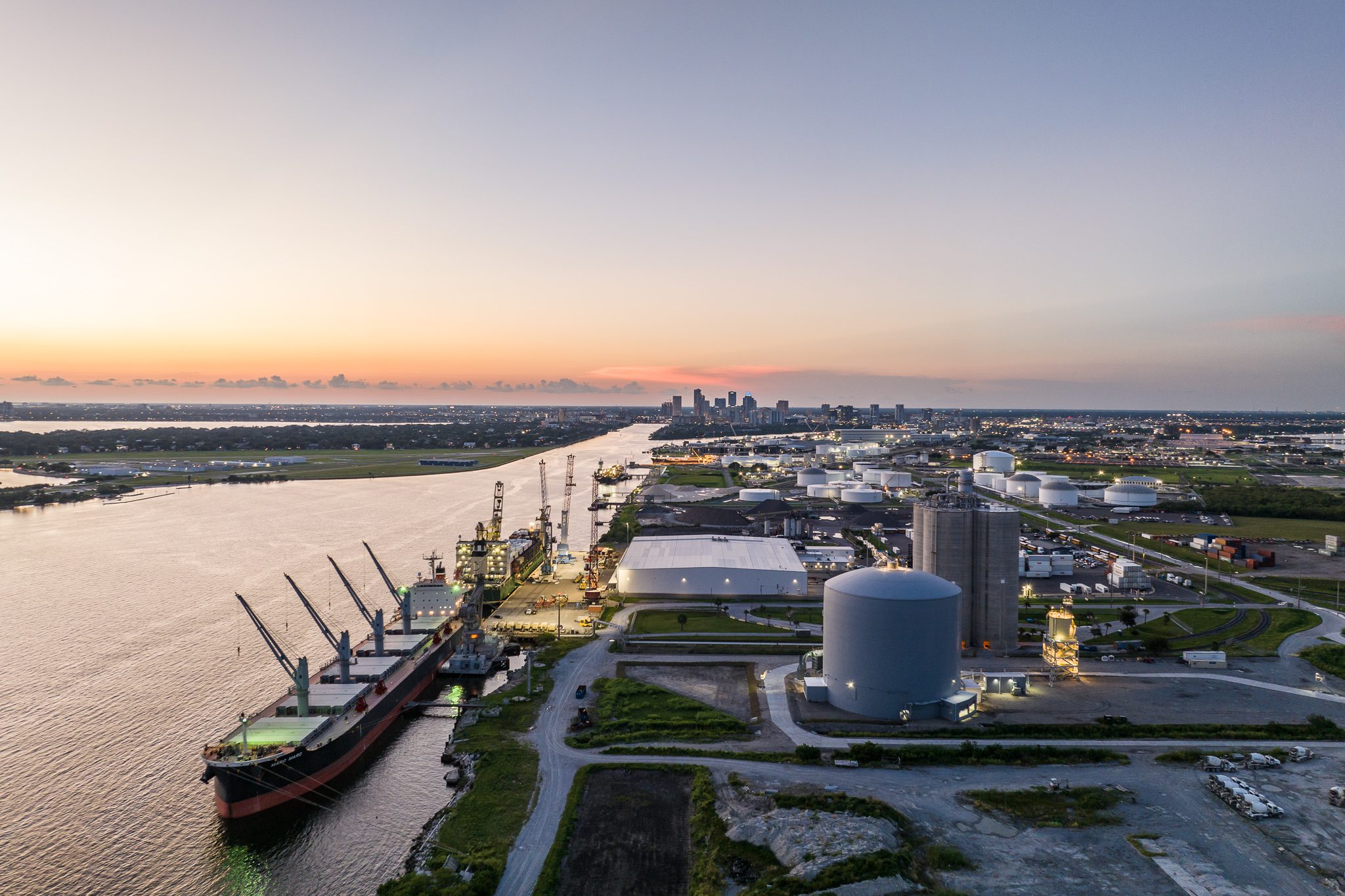 Aerial industrial photography of a Florida port terminal showing energy and logistics operations with cargo vessels and storage tanks at sunset.