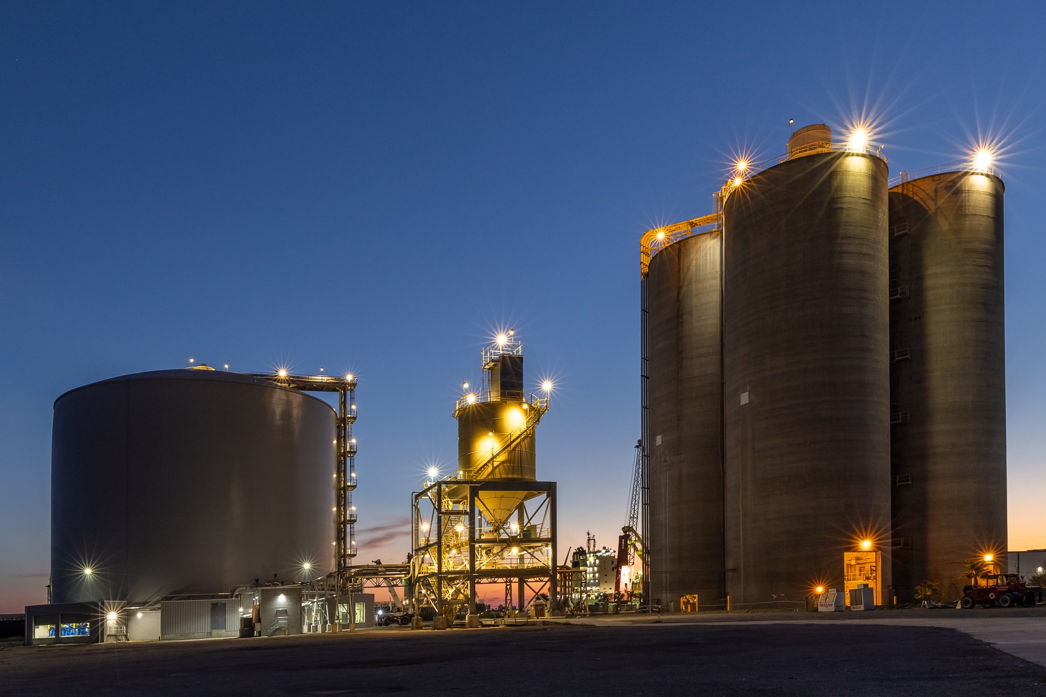 Industrial photography of bulk storage silos illuminated at dusk, representing large-scale infrastructure operations.
