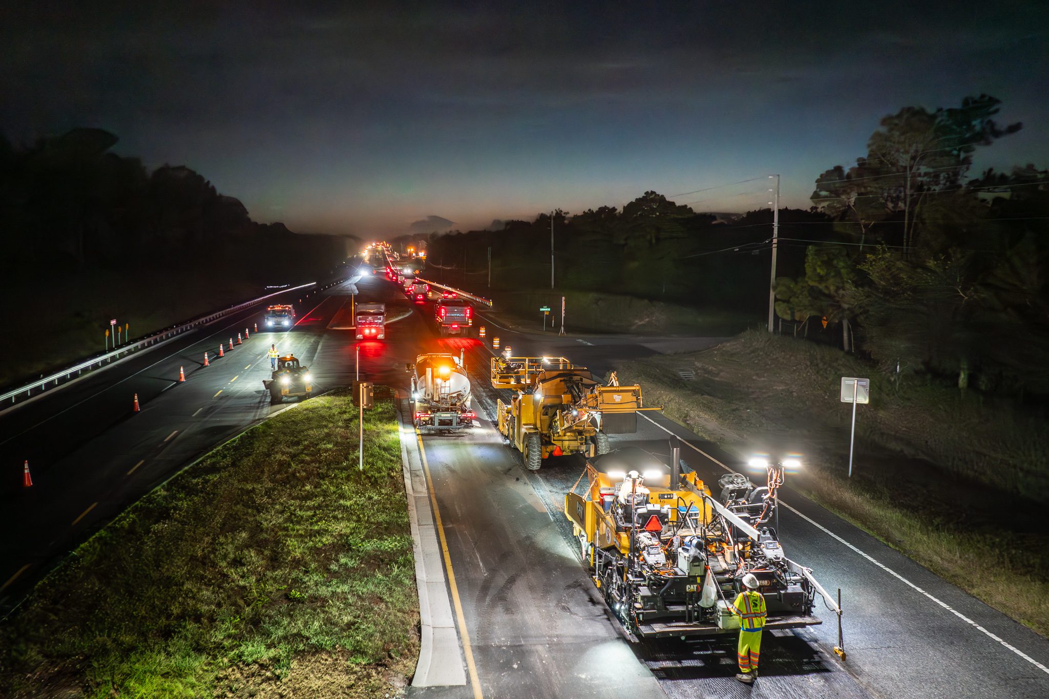 Nighttime industrial photography of road-paving crew working under lights.