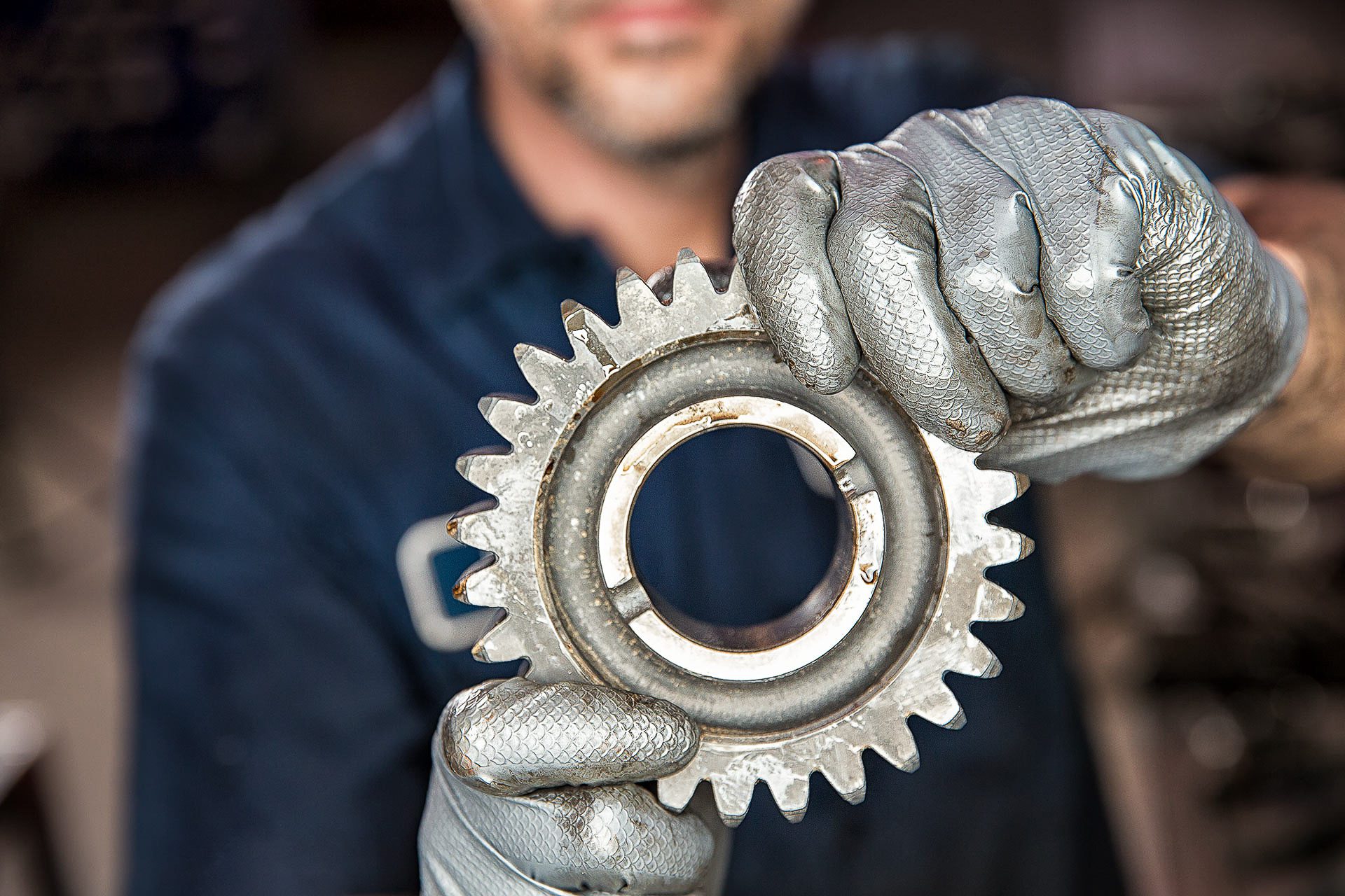 Close-up industrial photo of worker holding precision metal gear for maintenance.