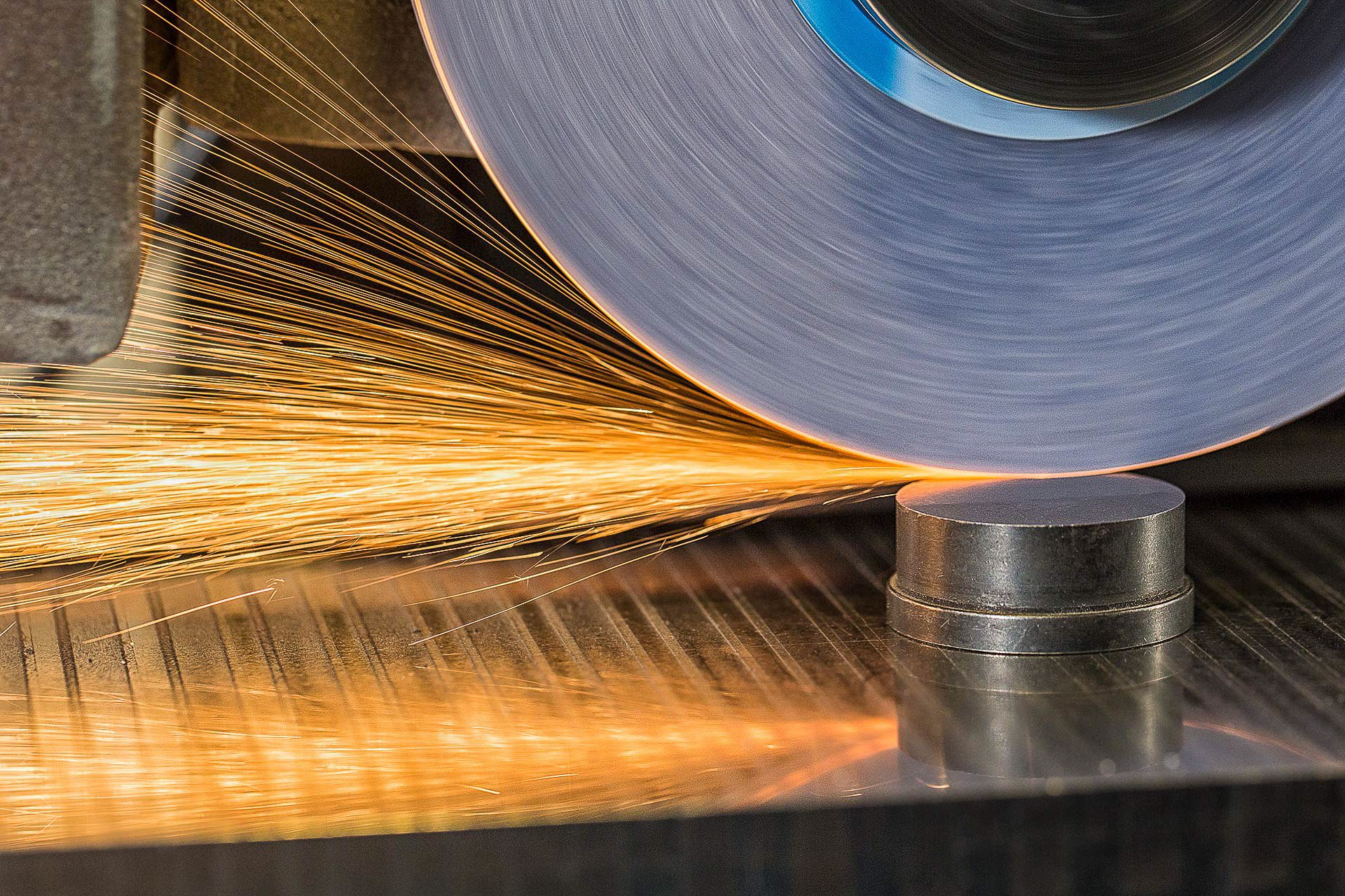 Industrial image of grinding wheel creating bright sparks on metal component.