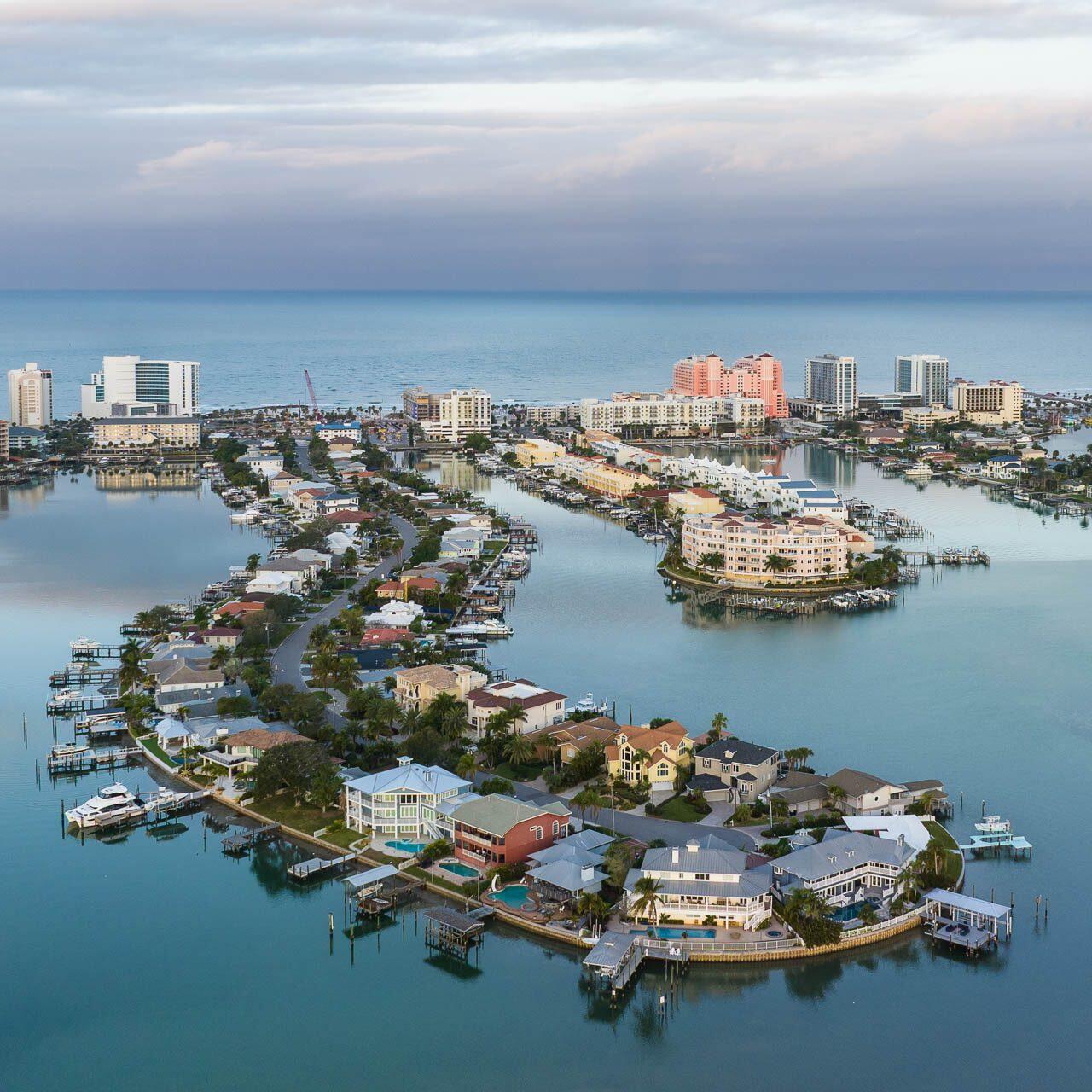 Aerial drone photograph of Clearwater Beach, Florida at sunrise showing waterfront homes, marinas, and resorts along the Gulf Coast.