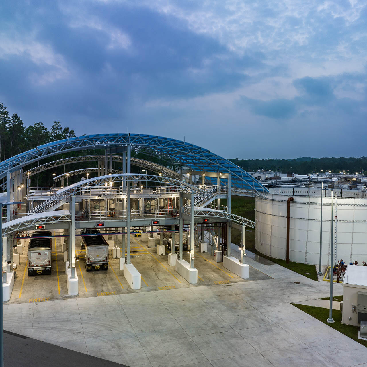 Aerial drone photograph of a Tampa Bay water treatment facility at dawn showing industrial tanks and truck bays under soft morning light.