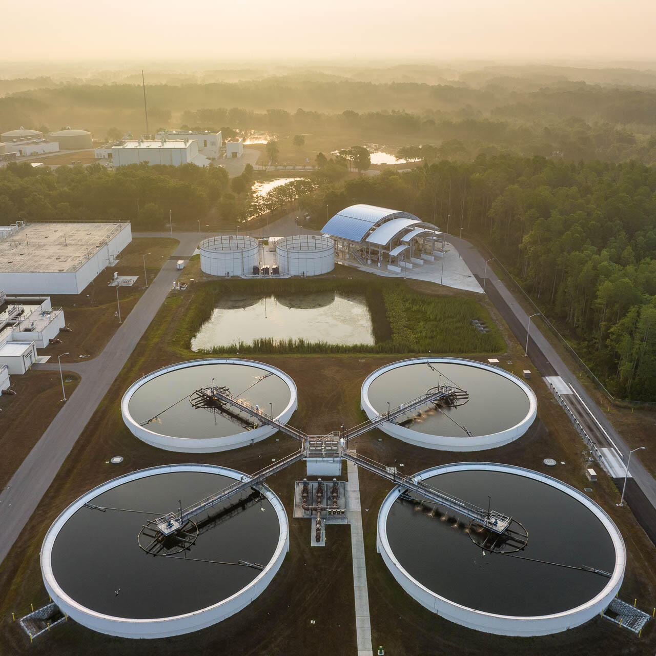 Aerial drone photograph of a Tampa Bay water treatment plant at sunrise with soft morning light and industrial structures surrounded by trees.
