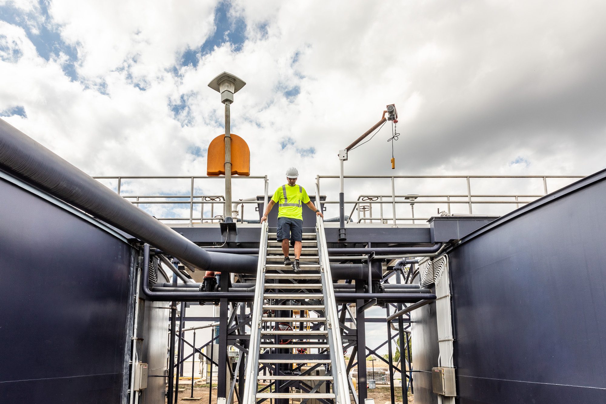 Technician descending access stairs between treatment tanks at water facility - industrial utility photography