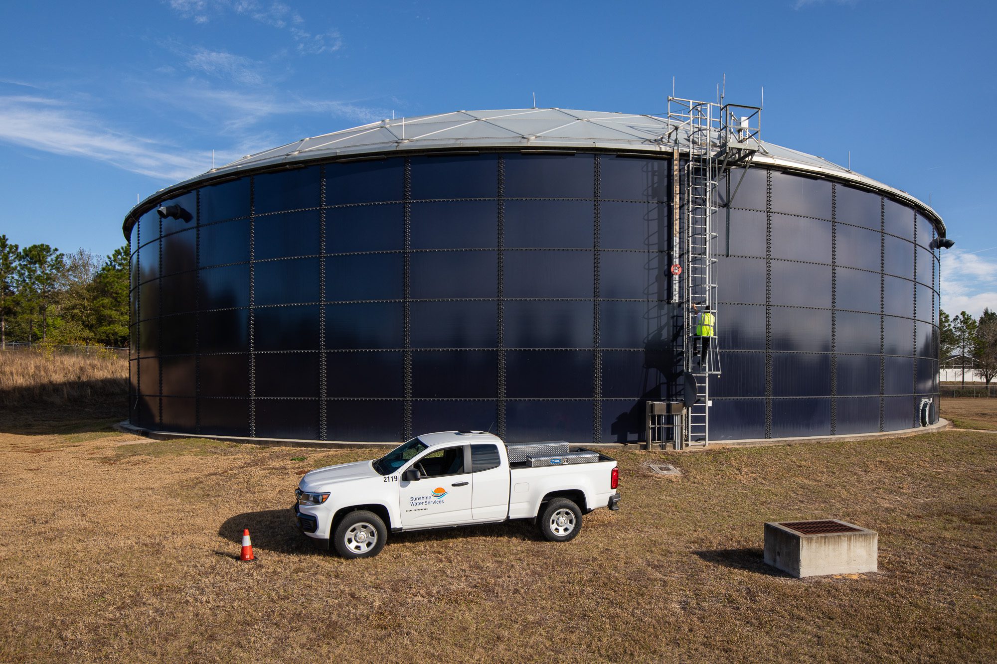 Large water storage tank with service truck and technician climbing ladder - utility infrastructure photography Florida
