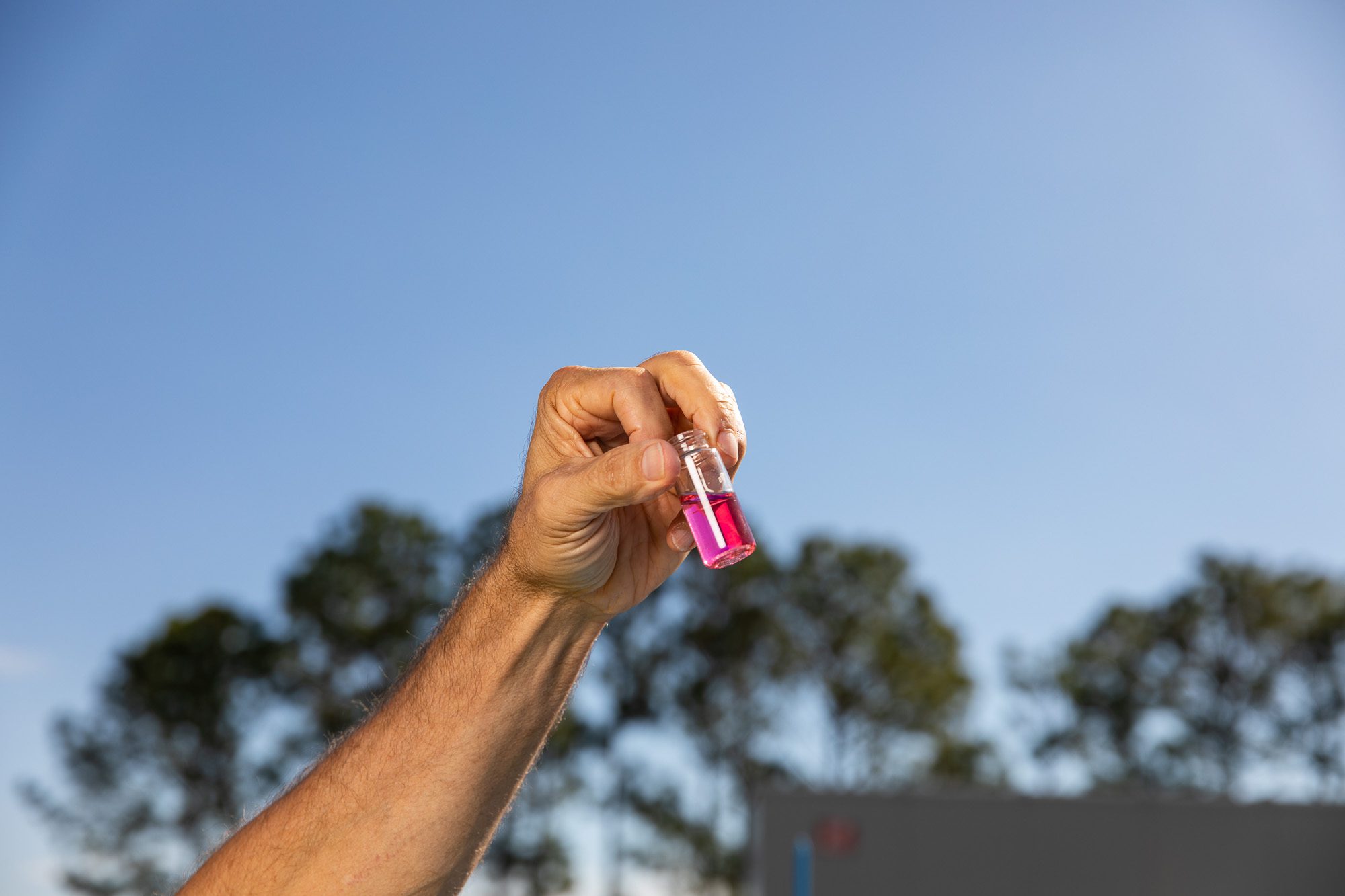 Water sample vial held up for testing against sky background - water quality testing photography